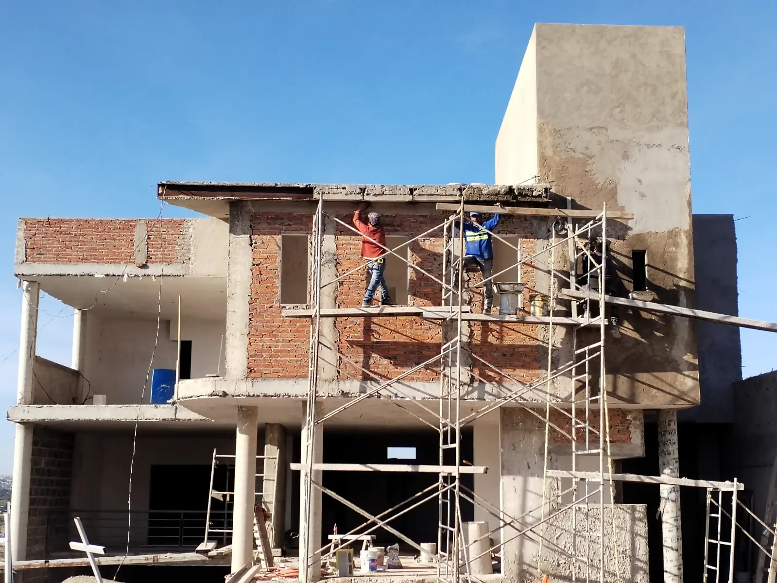 Trabajadores levantando muros de ladrillo sobre andamios